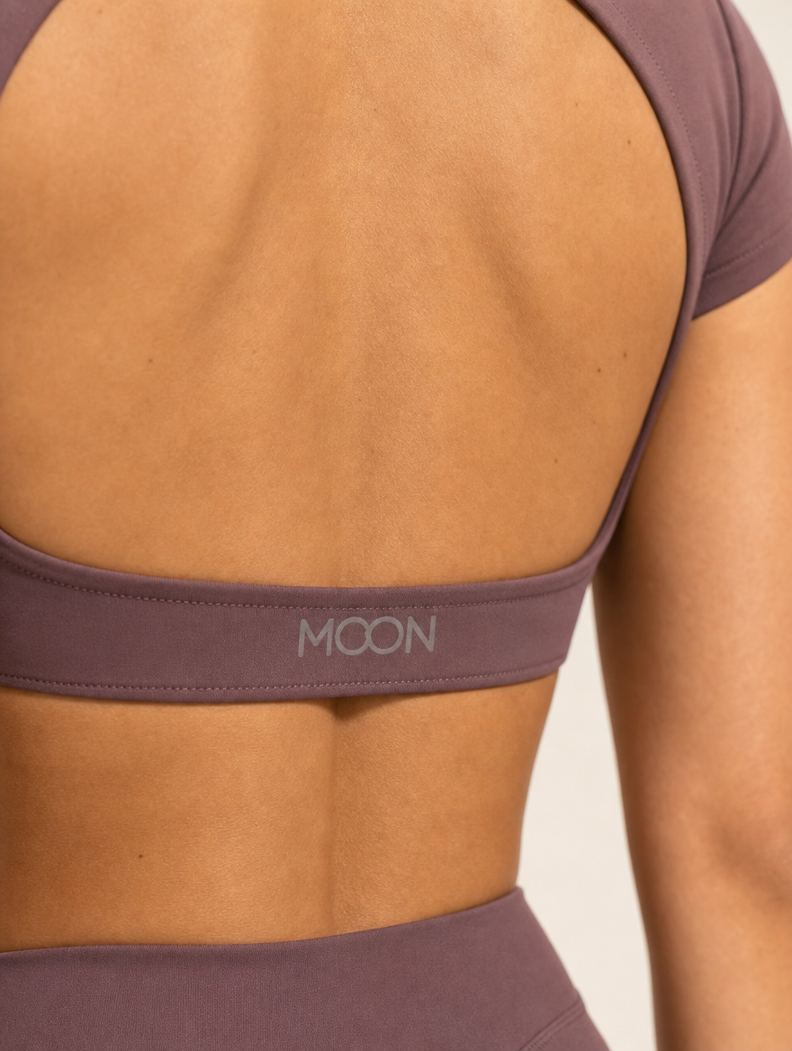 The Halo Set in Deep Umbra, close-up of the MOON logo on the back band and the shorts waistband, showing the matte stretch knit in deep plum.