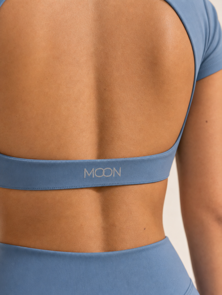 The Halo Set in Blue Hour, close-up of the MOON logo on the back band and the shorts waistband, showing the matte stretch knit in steel blue.