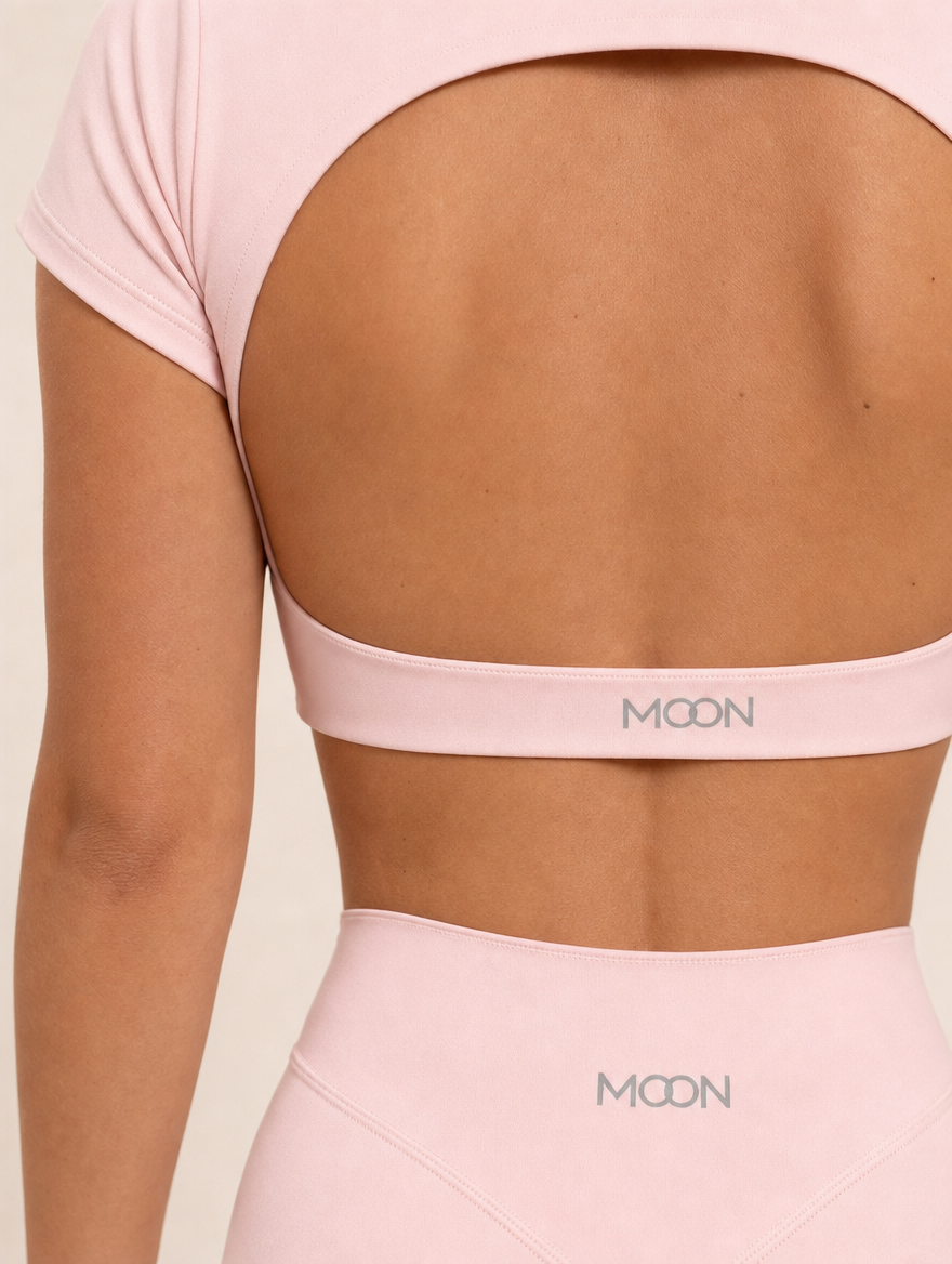 The Halo Set in Dawn Rose, close-up of the MOON logo on the back band and the shorts waistband, showing the matte stretch knit in soft pink.